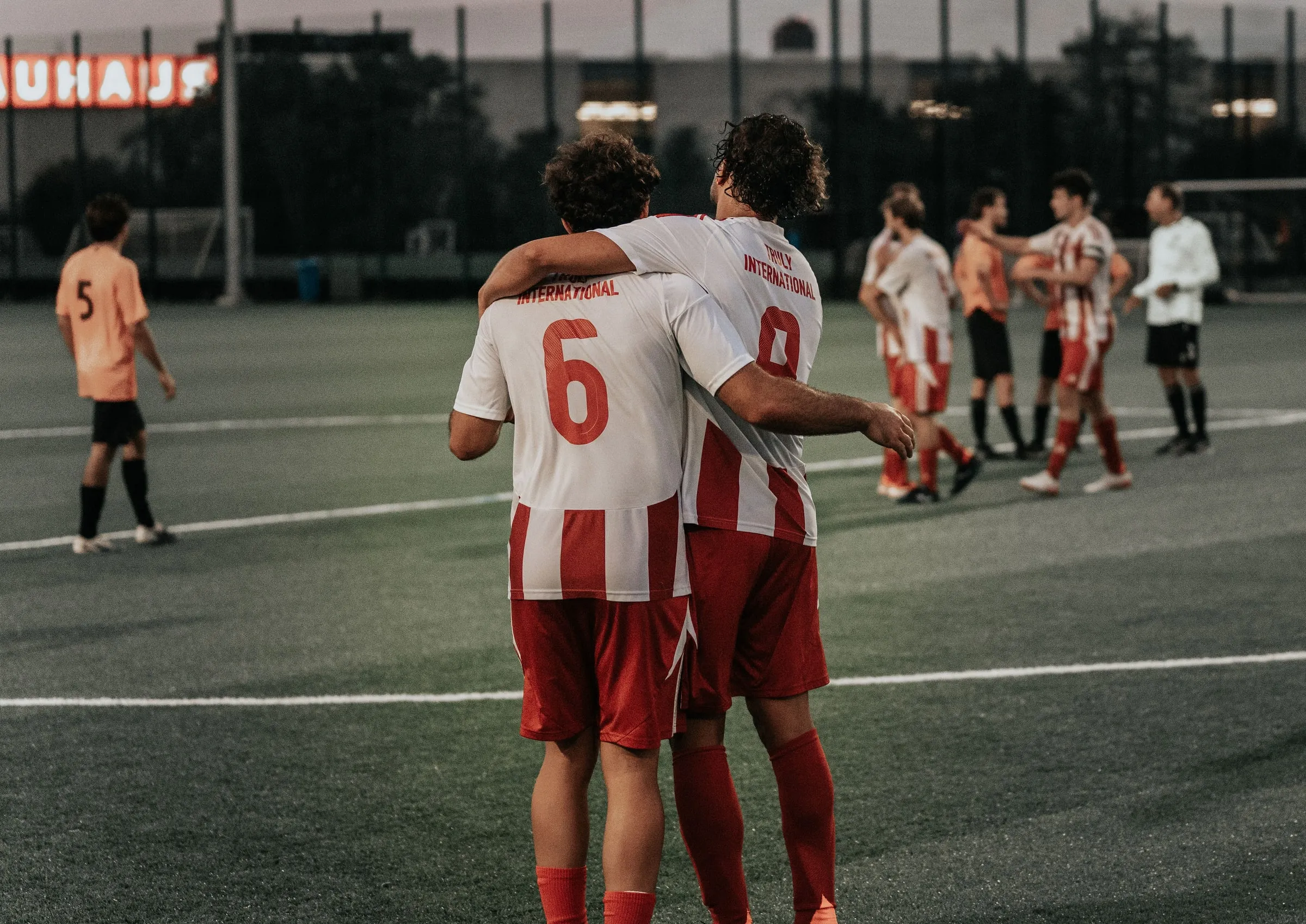Two teammates stand with their arms around each other's shoulders on the pitch