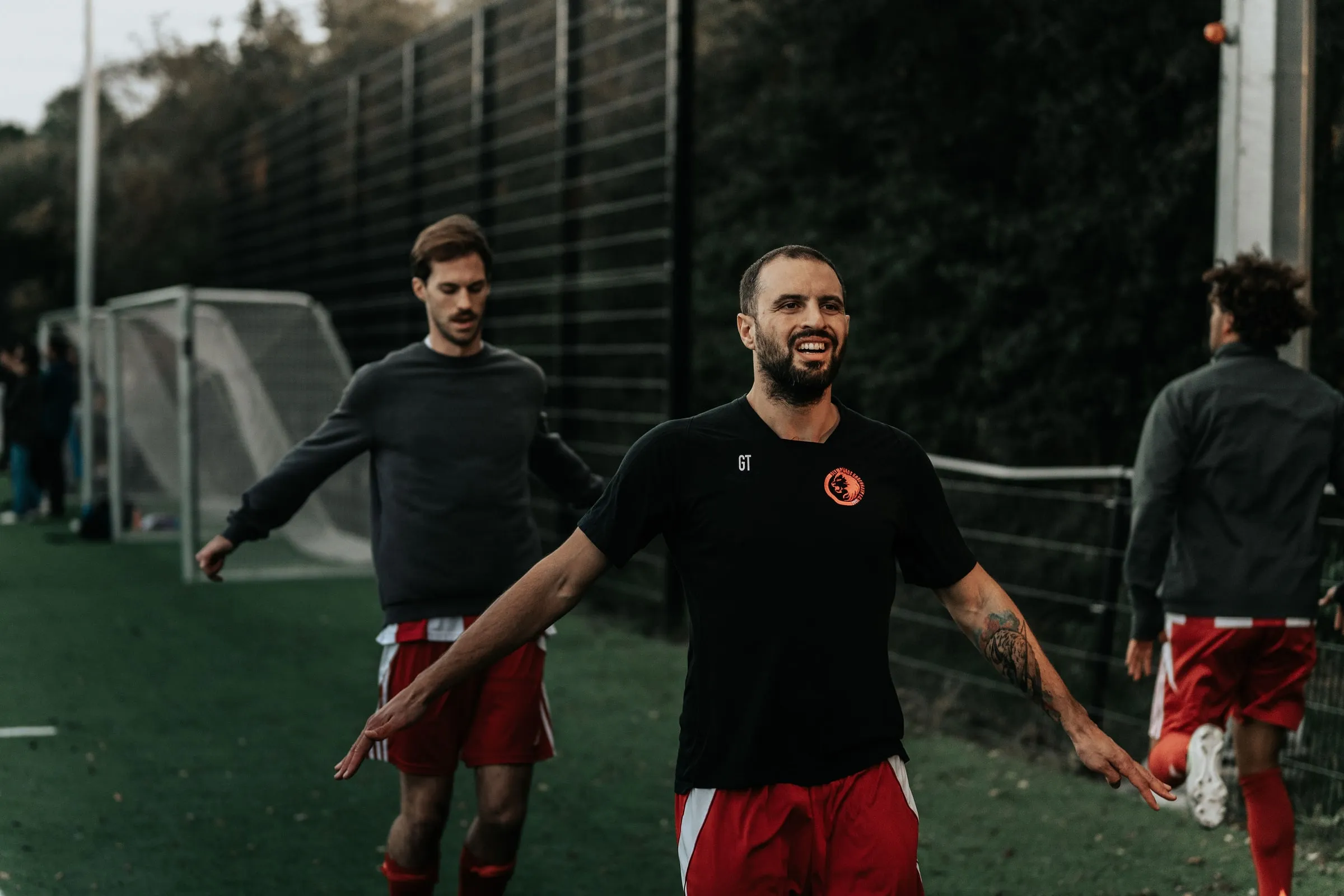 A player laughs with open arms while the team warms up next to the pitch