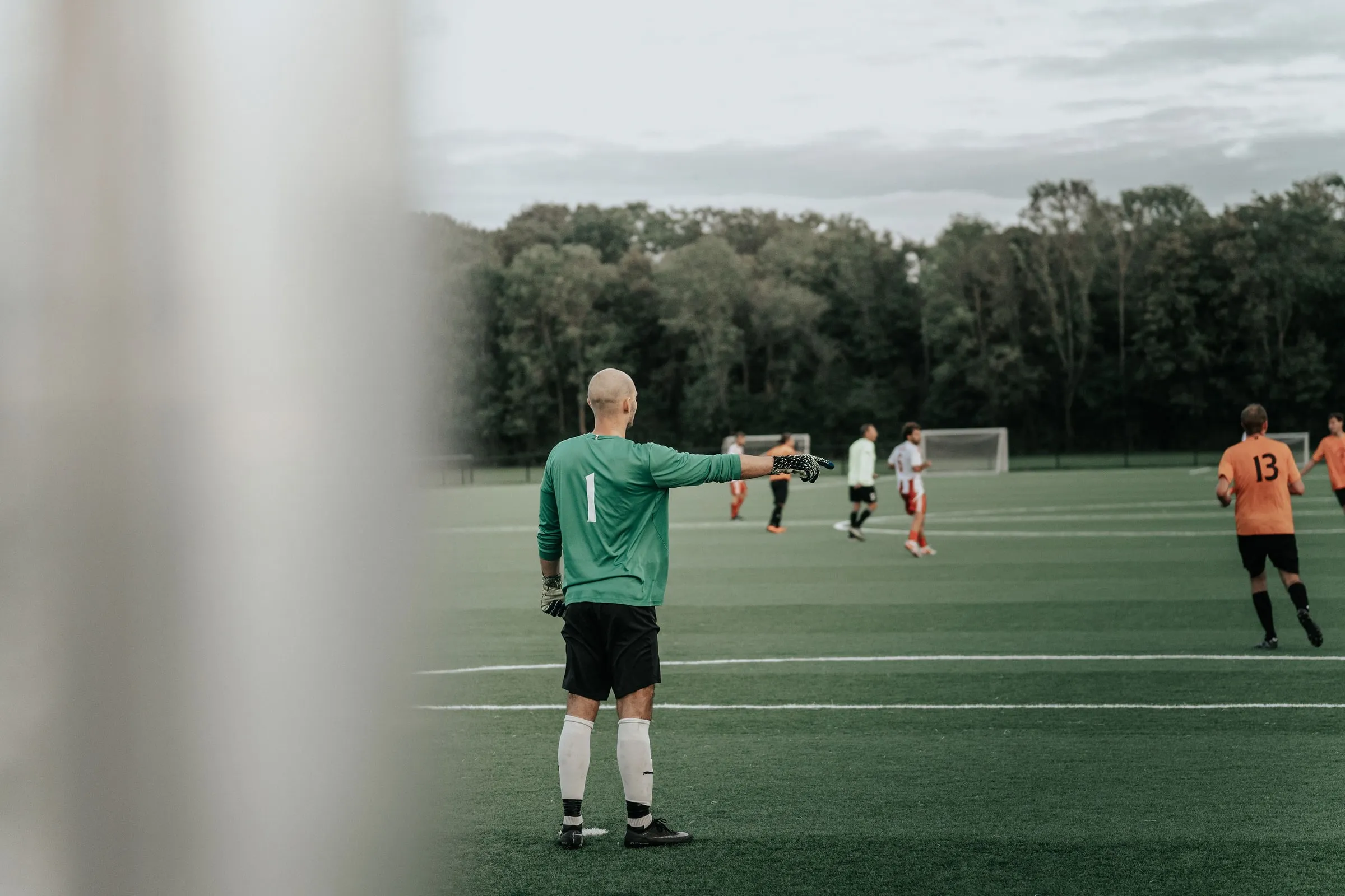 A goalkeeper in a green shirt points across the pitch during a match
