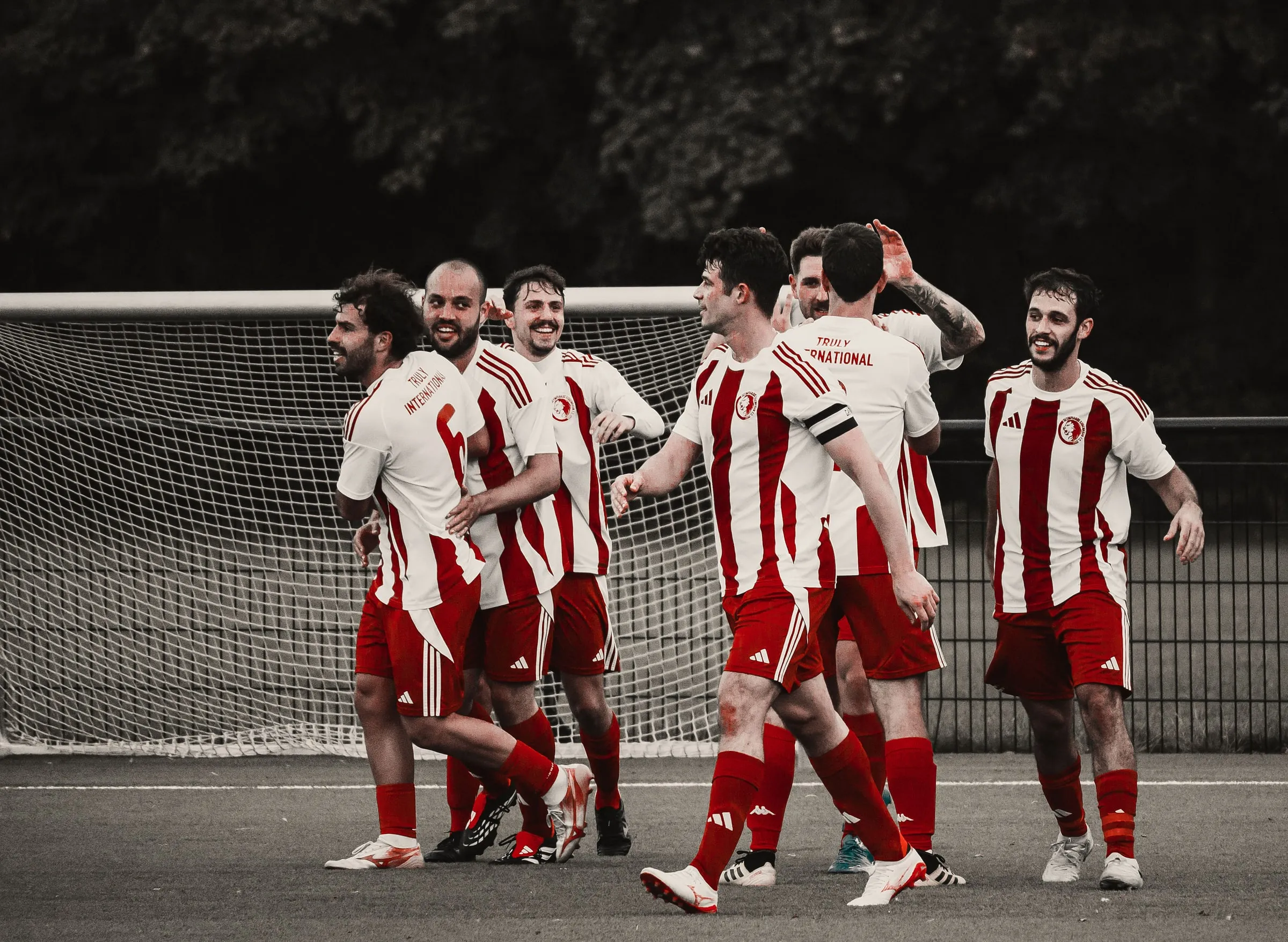A group of players in red and white striped shirts celebrate together in front of the goal